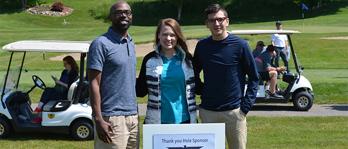 Golfers stand in front of a hole sponsor sign